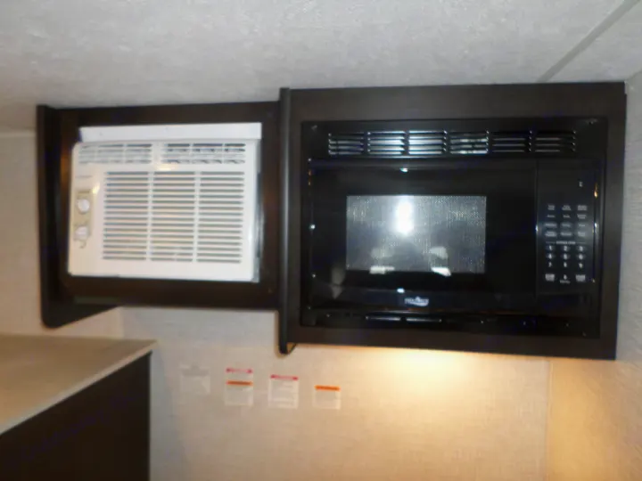 RV rental interior features an integrated white AC unit and black microwave in dark wood cabinets.. Braxton Creek Bushwhacker Plus 2022