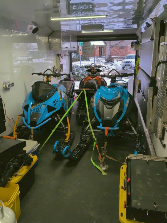 Two Arctic Cat snowmobiles are secured inside a transport trailer, prepared for winter adventures. Perfect for an RV rental trip!. Trails West RPM Toy Hauler 2023