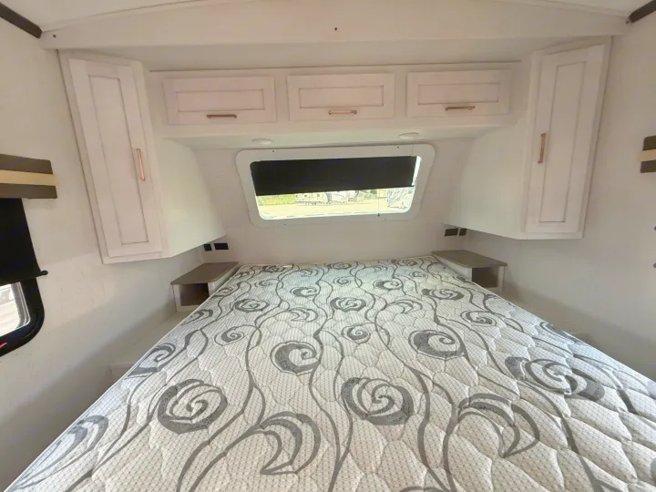 RV rental bedroom showcasing a comfortable bed with patterned mattress, overhead cabinets, and a window for natural light.. Astoria Astoria Trailer 2022