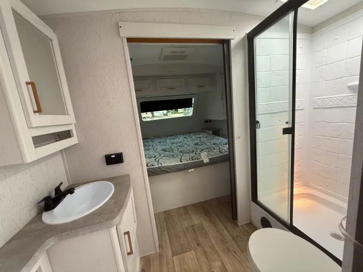 RV rental interior showcasing a bright, modern bathroom with shower and vanity, leading into a comfy bedroom.. Astoria Astoria Trailer 2022