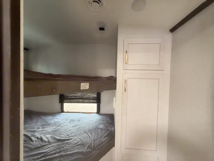 View inside an RV rental of a bunk room with two grey-sheeted beds, a window, and adjacent white cabinets.. Astoria Astoria Trailer 2022
