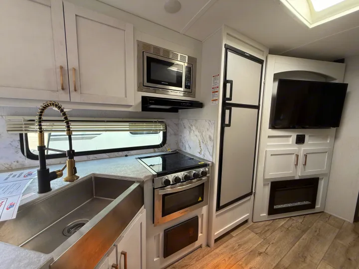 This modern RV kitchen, featuring sleek appliances, sink, and a cozy fireplace, is ideal for your next rv rental adventure.. Astoria Astoria Trailer 2022