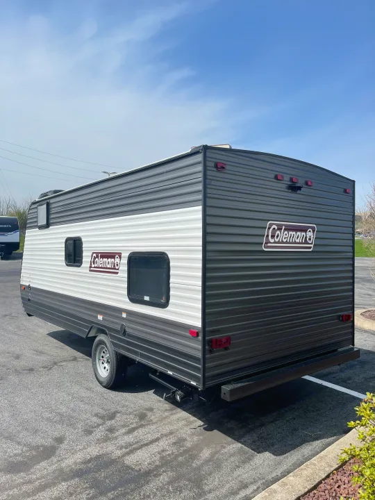 A gray and white Coleman travel trailer, well-suited for RV rental, is shown parked on a bright day. Note its compact size.. Dutchmen Coleman Lantern LT 2021