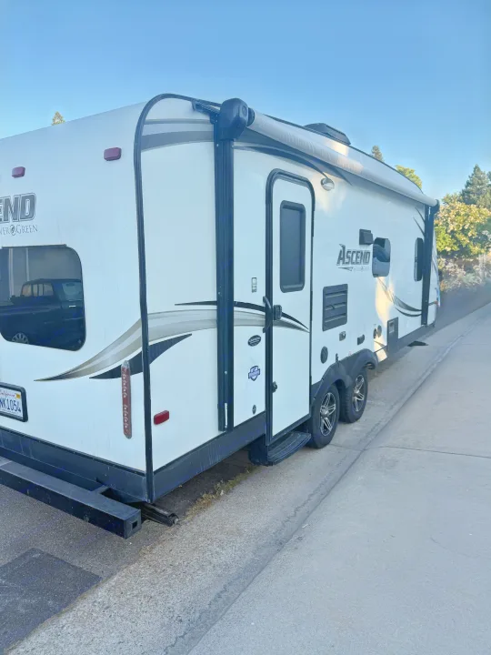 Spacious white travel trailer for **rv rental**, ideal for road trips & camping. Features an awning and multiple windows.. Evergreen RV Ascend 2015