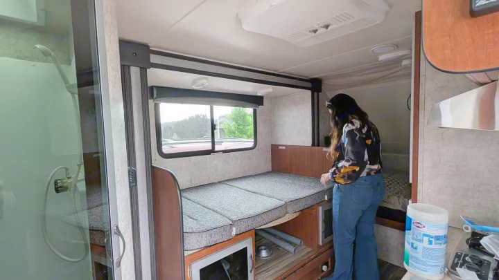 An RV rental's adaptable interior: a woman stands near the convertible bed, with a full shower to the left.. Travel Lite Falcon 2018