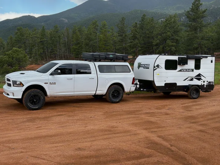 White truck towing a Viking travel trailer, ready for an RV rental off-road adventure in the mountains.. Forest River Viking 12000 2024