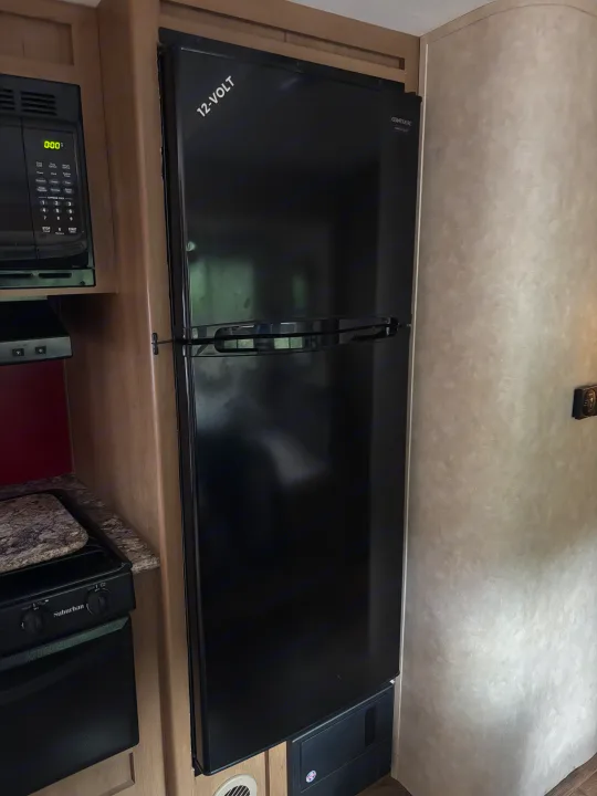 Compact RV rental kitchen featuring a black 12-volt refrigerator, microwave, and stove/oven setup.. Cruiser Rv Corp 280Bunkhouse Cruiser 2015