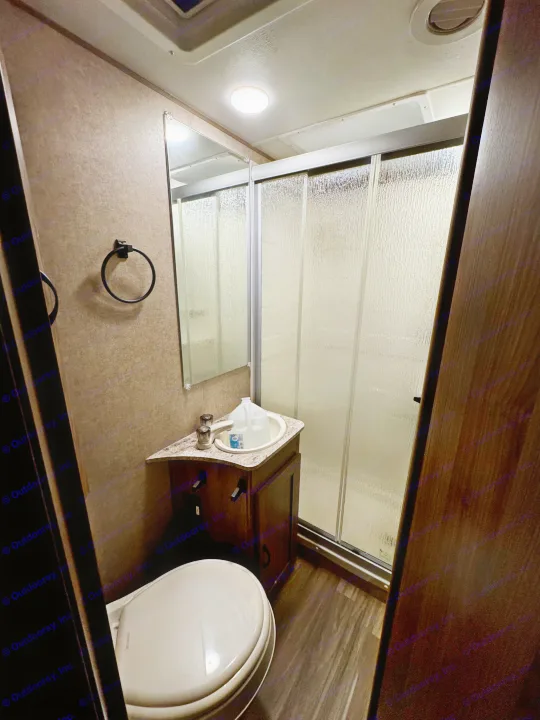 This compact RV rental bathroom features a toilet, sink vanity with a mirror, and a glass-door shower stall.. Forest River Coachmen Freelander 2017