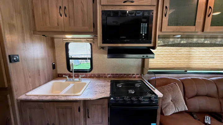 Clean RV rental interior: well-equipped kitchen with microwave, stove, sink, plus a comfy brown couch for your travel adventures.. Forest River Coachmen Freelander 2017