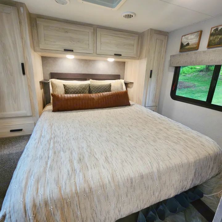 Cozy RV rental bedroom with striped bedding, overhead storage, and a window offering green views. Ready for travel.. Forest River Sunseeker LE 2022