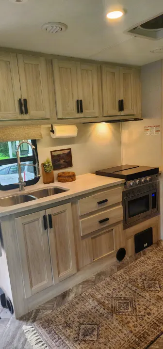 Modern RV rental kitchen with light wood cabinets, double sink, stove, and microwave. Compact and functional space.. Forest River Sunseeker LE 2022