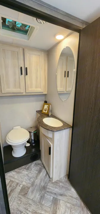 Clean RV rental bathroom featuring toilet, vanity with sink, overhead cabinets, mirror, and ceiling vent for comfort.. Forest River Sunseeker LE 2022