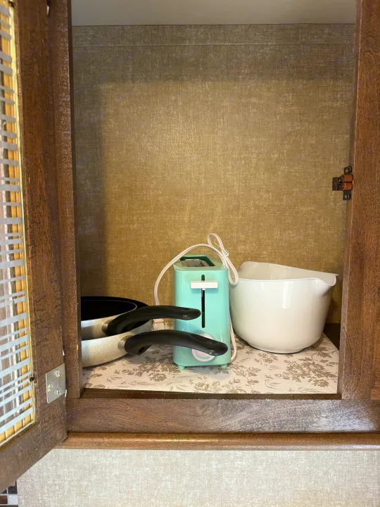Open RV rental kitchen cabinet, neatly stocked with cooking pans, a mini toaster, and a mixing bowl on a patterned liner.. Forest River Vibe Extreme Lite 2017