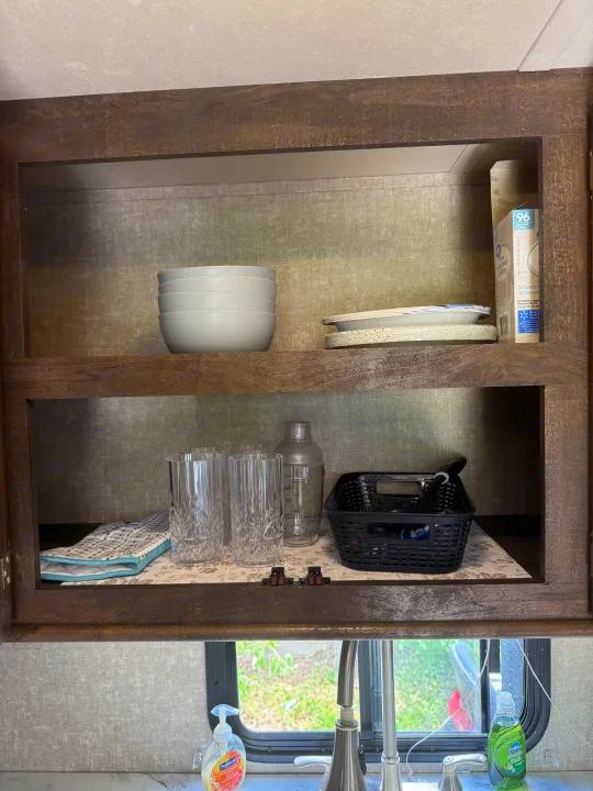 Inside an RV rental: a neatly stocked kitchen cabinet with bowls, paper plates, cutlery, drinking glasses, and a cocktail shaker.. Forest River Vibe Extreme Lite 2017