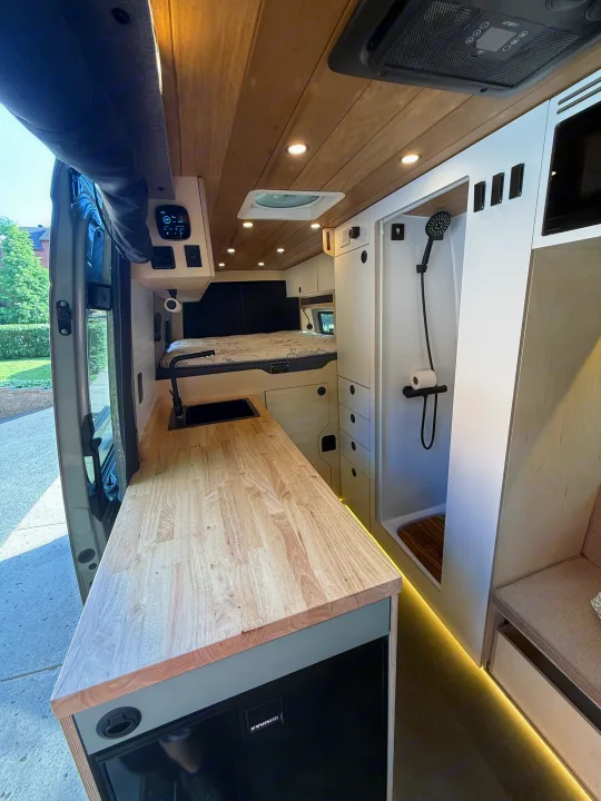 Explore this modern RV rental camper van interior, featuring a sleek kitchen, cozy bed, and integrated shower for road trips.. Mercedes-Benz sprinter 2024