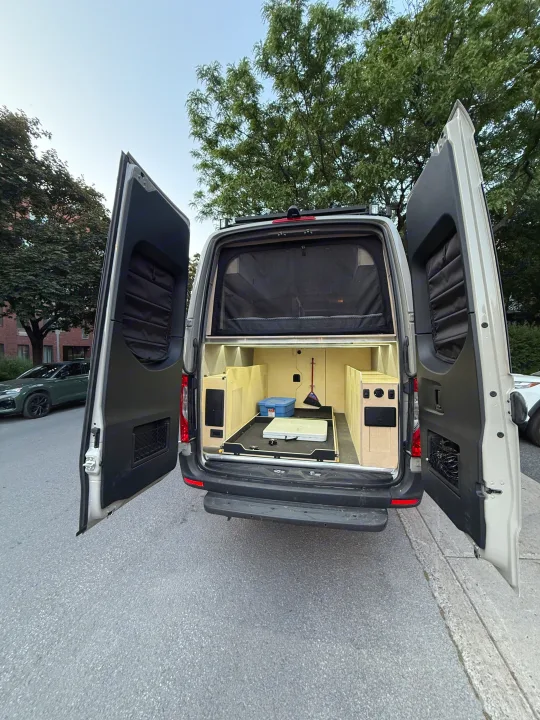 Open rear of a custom camper van, showcasing an organized interior with pull-out storage. Perfect for RV rental trips!. Mercedes-Benz sprinter 2024