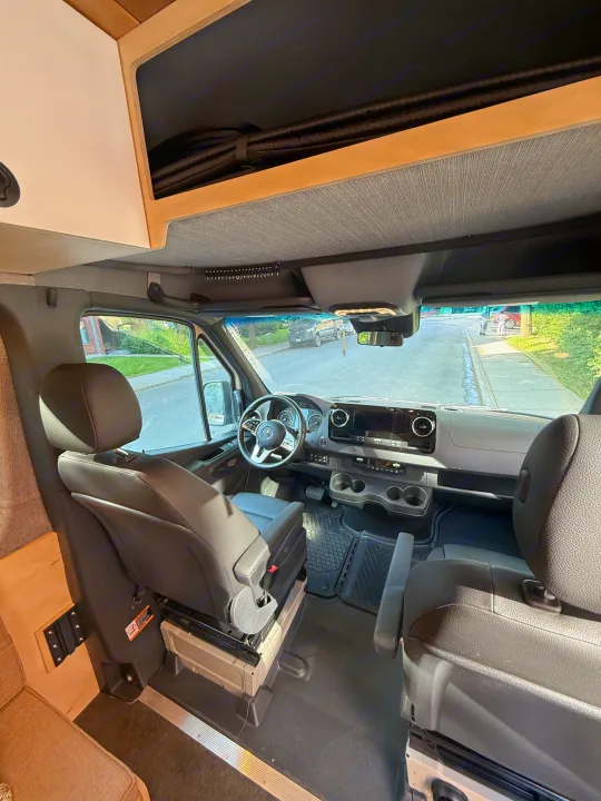 RV rental: Inside a modern Sprinter camper van, showing the driver's cabin, dashboard, and custom overhead storage.. Mercedes-Benz sprinter 2024
