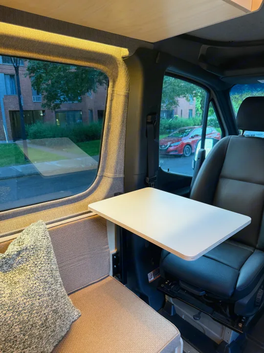 Cozy RV rental interior featuring a versatile table, comfortable seating, and scenic window views of the outside.. Mercedes-Benz sprinter 2024