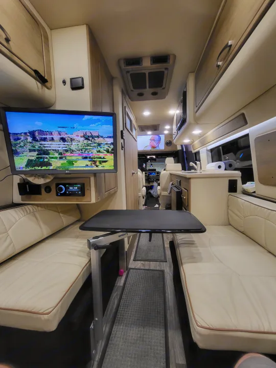 Spacious RV rental interior with versatile dining table, side seating, and entertainment screens.. Midwest Automotive Designs American Patriot 2022