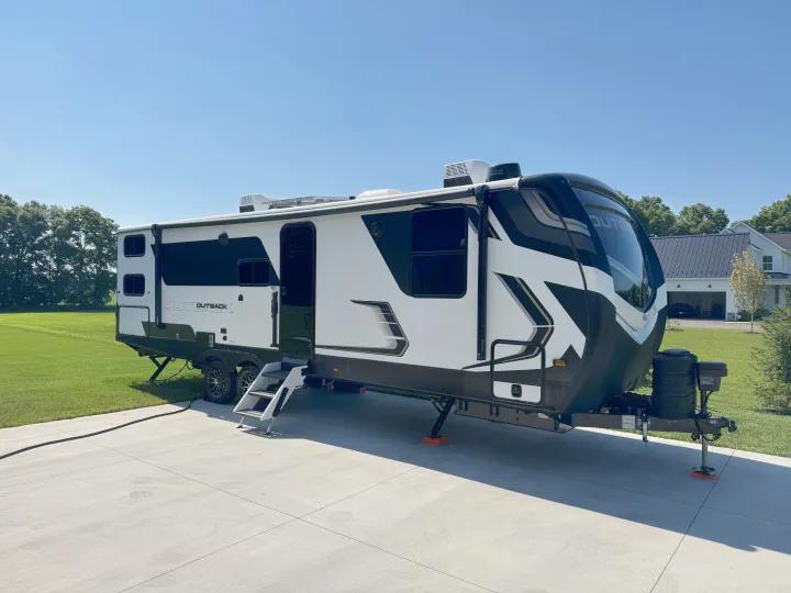This large, modern Outback travel trailer RV rental is set up on a sunny driveway, perfect for your next trip.. Keystone Outback 291BH 2025