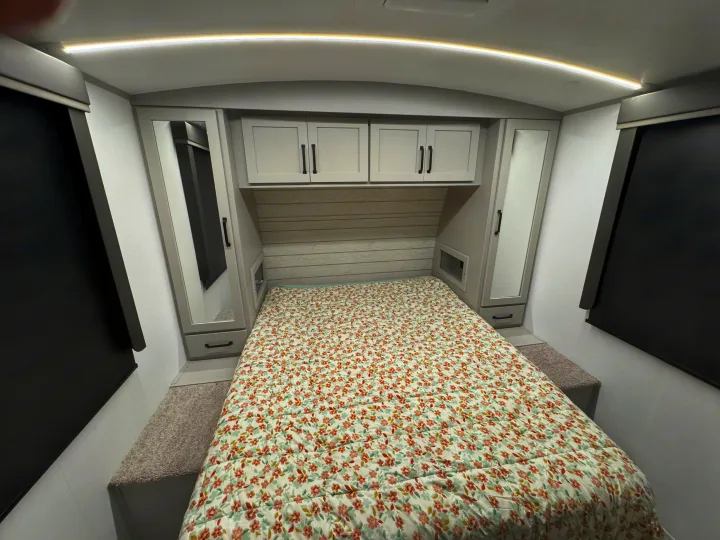 Cozy RV rental bedroom with floral bedding, overhead storage, mirrored wardrobes, and blackout blinds.. Keystone Outback 291BH 2025