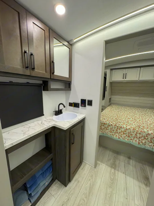 Inside a spacious RV rental: a modern vanity, organized storage, and cozy bedroom with floral bedding.. Keystone Outback 291BH 2025