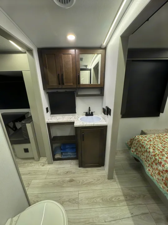 Inside a modern RV rental: a compact bathroom vanity with storage, sink, and glimpse of the adjacent bedroom and living space.. Keystone Outback 291BH 2025