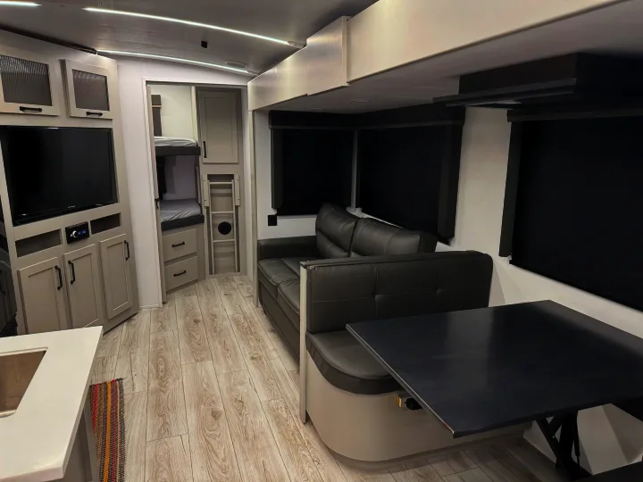 Modern RV rental interior: living area with sofa, dining booth, TV, and bunk beds in a light, modern design.. Keystone Outback 291BH 2025