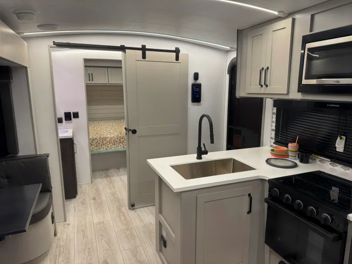 RV rental: Sleek kitchen with sink/stove, dining booth, and private bedroom behind a barn door.. Keystone Outback 291BH 2025