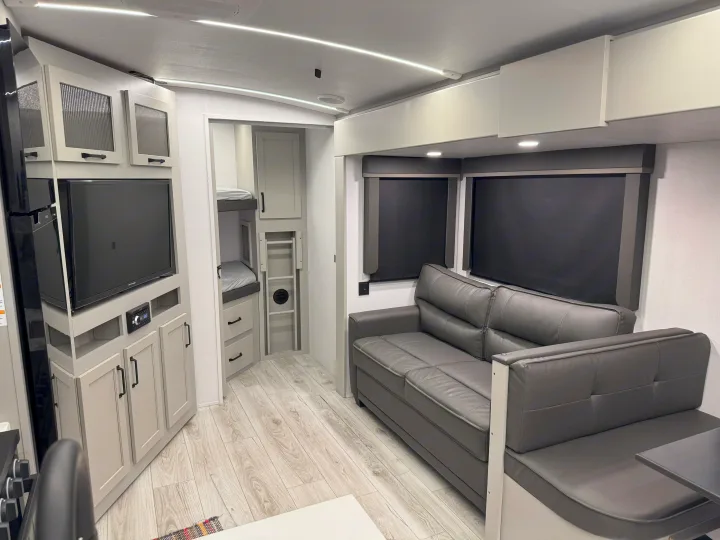 Clean, modern RV rental interior with a grey sofa, entertainment center, and bunk beds for comfortable travel.. Keystone Outback 291BH 2025