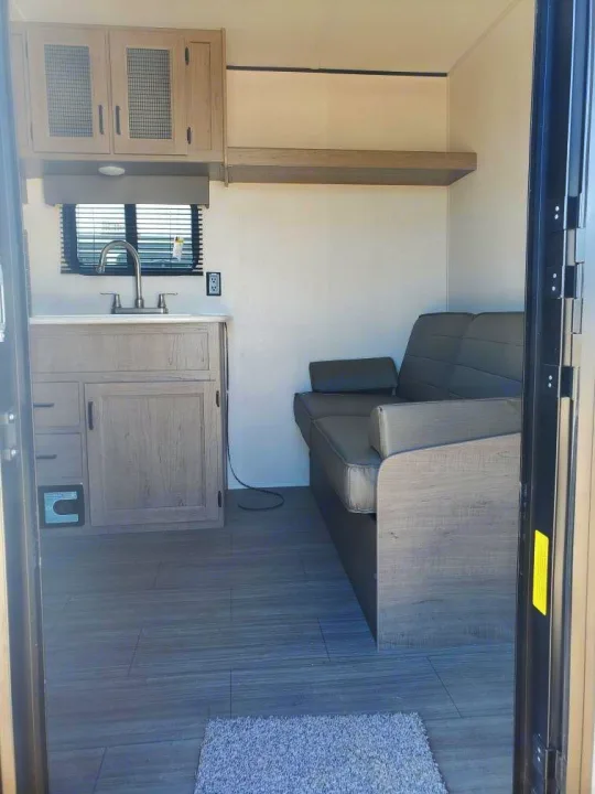 RV rental interior: Bright, modern space with a compact kitchen (sink, cabinets) and a cozy sofa, seen from the entrance.. Keystone RV Hideout 2021