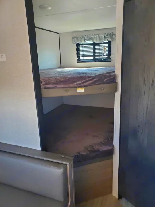Inside an RV rental: a bright interior shows cozy bunk beds, a window, and a seating area. Perfect for family camping.. Keystone RV Hideout 2021