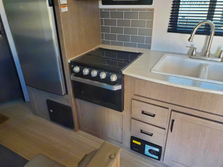 This RV rental showcases a compact kitchen area with a stainless steel refrigerator, stovetop, oven, and sink for your adventures.. Keystone RV Hideout 2021