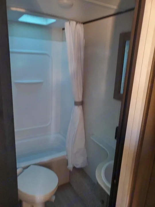 Compact RV rental bathroom: white tub/shower combo, toilet, small sink, and overhead skylight for your travels.. Keystone RV Hideout 2021
