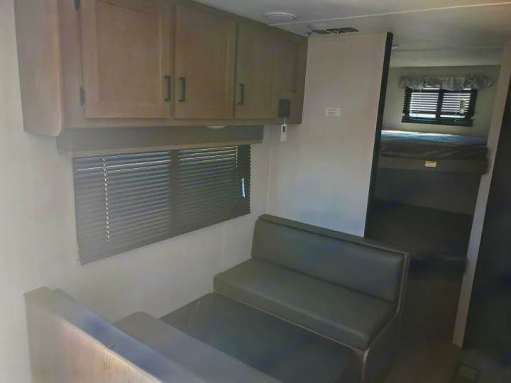 RV rental: view inside a travel trailer showing dinette seating, wall cabinets, and bunk beds in a separate sleeping area.. Keystone RV Hideout 2021