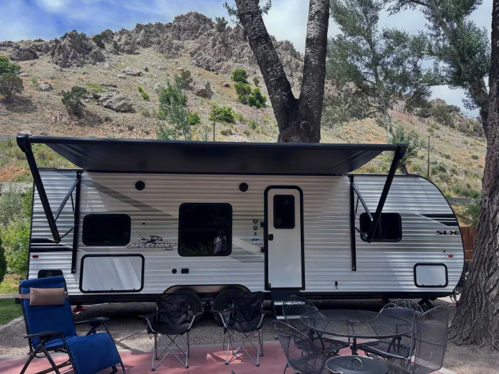 RV rental setup at a mountain campsite, featuring a travel trailer with extended awning, patio seating, and scenic rocky hills.. Jayco Jay Flight slx 260 bhw 2025