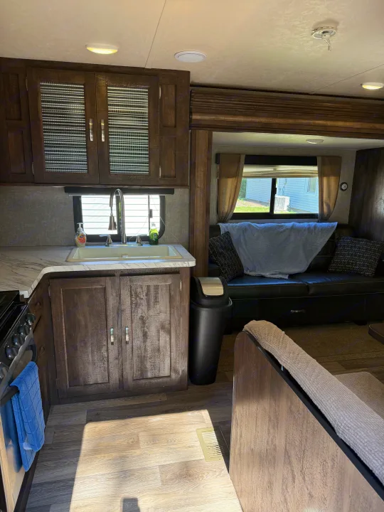 RV rental interior: light wood-look floor, modern kitchen with sink, and dark leather couch in a cozy living area.. Forest River Vibe Extreme Lite 2017