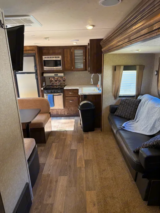 Modern RV rental interior: kitchen with microwave & sink, dining booth, and cozy living area with sofa & TV. Ideal for trips.. Forest River Vibe Extreme Lite 2017