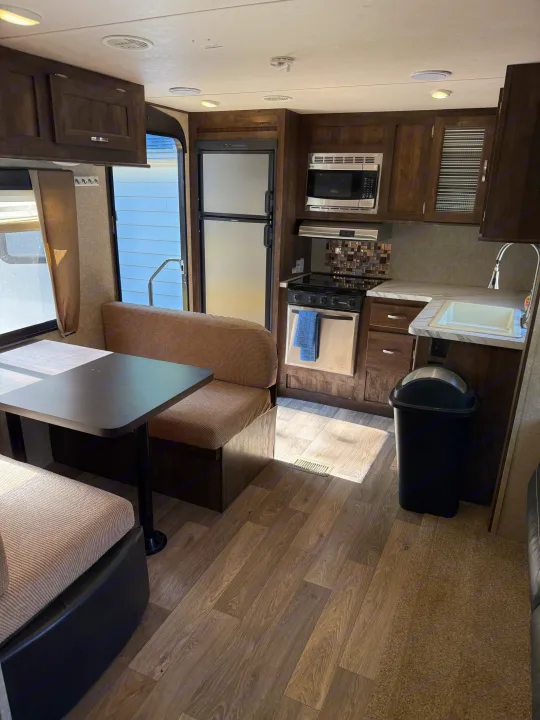 Cozy RV rental interior with a dinette, functional kitchen including fridge, microwave, stove, and sink, on wood-look flooring.. Forest River Vibe Extreme Lite 2017