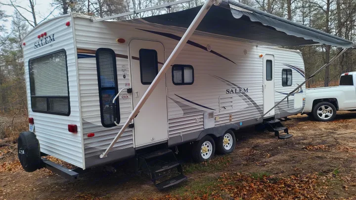 Parked white Salem RV with an extended black awning and steps down, suggesting a ready rv rental in a wooded area.. Coachmen salem 2013
