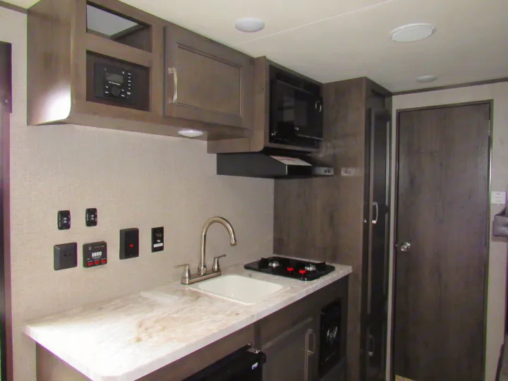 RV rental kitchen interior featuring a compact sink, stove, microwave, and modern cabinetry with integrated controls, ideal for travel.. Jayco Jay Flight SLX 2021