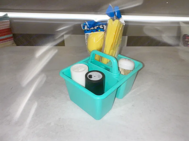 Teal caddy holding yellow plastic cutlery, shakers, and toothpicks, ready for your RV rental kitchen.. Forest River Wildwood X-Lite 2022