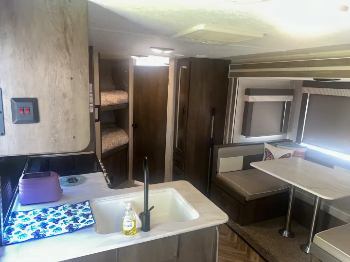 Interior view of an RV rental: kitchen with sink, bunk beds, and dining area with table and seats.. Forest River Wildwood X-Lite 2022