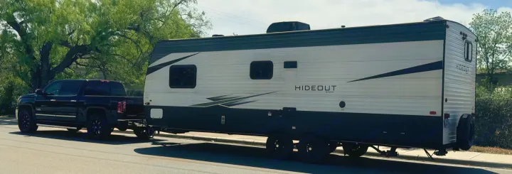 Black pickup truck towing a white and dark grey Hideout travel trailer, an ideal RV rental for your next adventure.. Keystone RV Hideout 2021