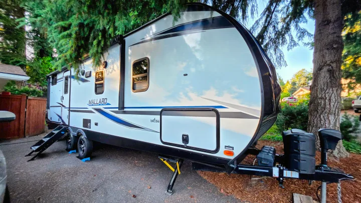 A modern white and black travel trailer, possibly for RV rental, is parked outside, set up for camping.. Heartland RVs Mallard 2021