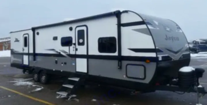 This sleek white and gray travel trailer is perfect for an **rv rental** adventure, parked outdoors in the snow.. Jayco Jay Flight SLX 2024