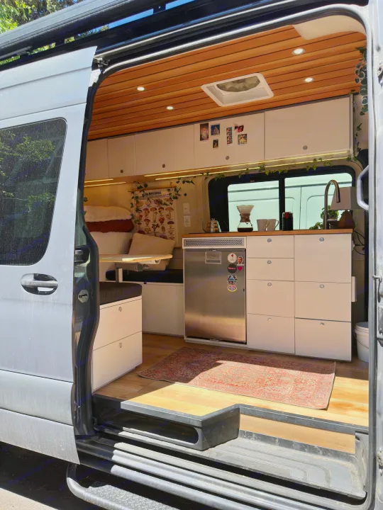 Explore this modern RV rental's cozy interior, featuring a full kitchen, bed, and seating area. Ideal for van life adventures.. Mercedes-Benz Sprinter 2021
