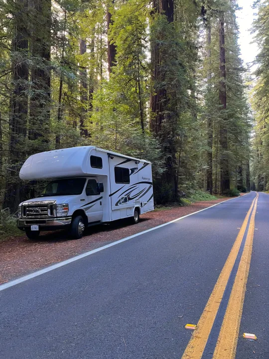 A white RV rental is parked on the shoulder of a road, flanked by towering redwood trees, inviting forest adventures.. Forest River Forester Classic 2291S 2020