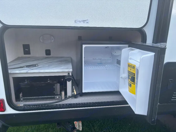 This RV rental's outdoor kitchen reveals a mini-fridge, pull-out grill, and counter, ideal for camping adventures.. Coachmen Apex 2025