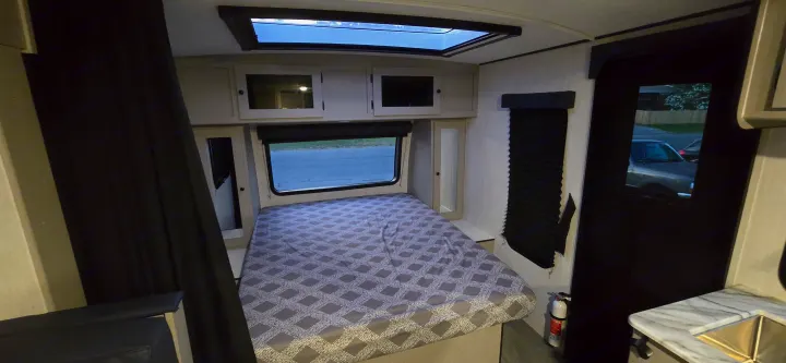 Spacious RV rental bedroom showcasing a comfortable bed, overhead skylight, large window, and visible fire extinguisher.. Coachmen Apex 2025